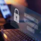 It features a close-up of a laptop with a transparent digital login interface layered on top. This interface prominently displays a padlock icon, symbolizing security, alongside fields for a username and a password (hidden by asterisks).