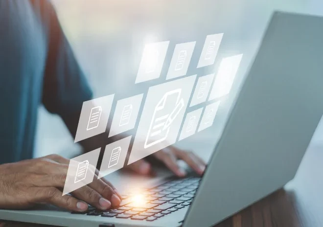 A close-up of a person's hands typing on a laptop, with a bright, warm glow emanating from the keyboard. Floating above the laptop is a transparent digital interface displaying a workflow of glowing document icons.