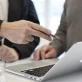 Two IT professionals discussing information displayed on a laptop screen, with one person pointing at the screen using a pen during a collaborative meeting.